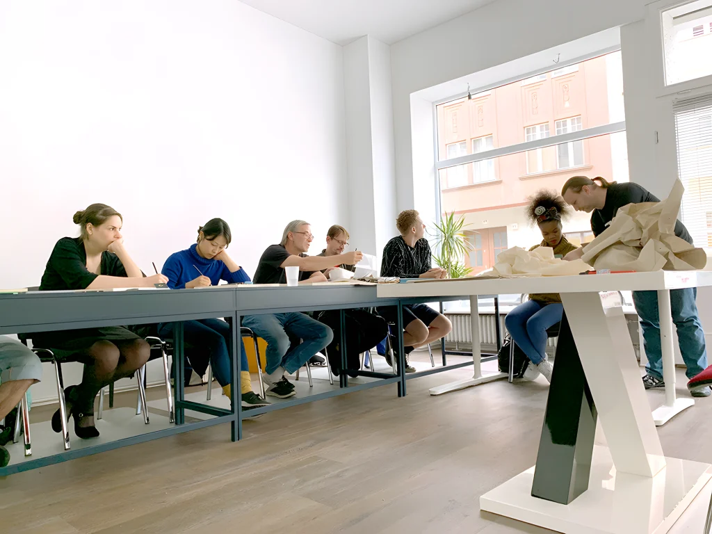 Teilnehmende arbeiten bei artsLab an langen Tischen an gestalterischen Aufgaben.